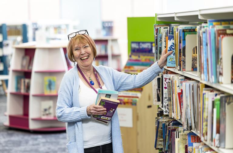 A lady smiling and looking at books in Wokingham Library