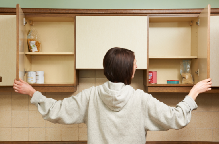 A woman opens two kitchen cupboards showing a few tinned goods left at the back of the cupbard