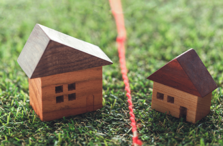 Two small wooden houses on grass with a red line dividing them