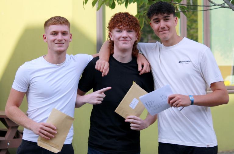 Three boys from Waingels College stand with their arms round each other holding their exam results up