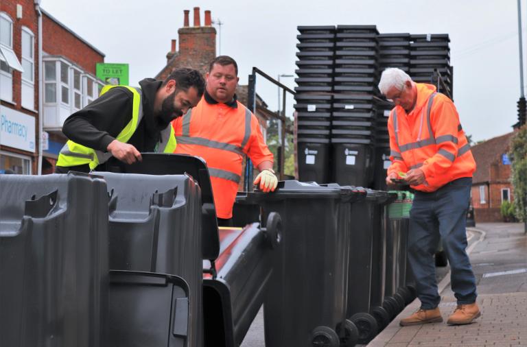 Three men in high vis jackets assemble bins in Twyford high street by attaching the wheels