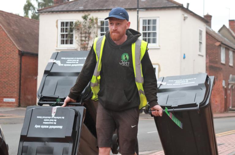 A bin delivery man in a high vis vest wheels four bins along the street in Wokingham town centre