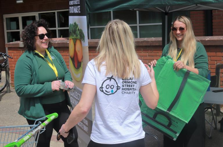 Two smiling women from the council hand a green recycling bag to a shopper from a stall outside Asda in Lower Earley