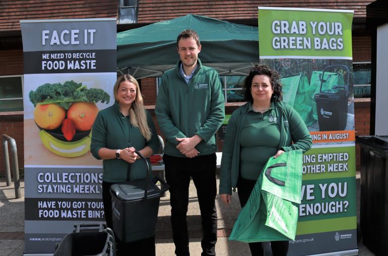 Two women and a man from the council's recycling team smile and hold various waste containers at their stall outside Asda in Lower Earley