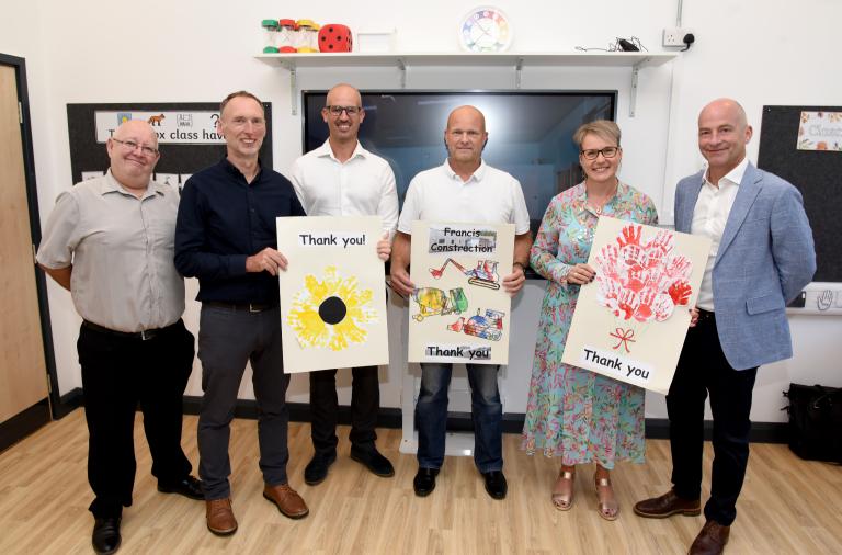 Six adults pose with large thank you cards made by children