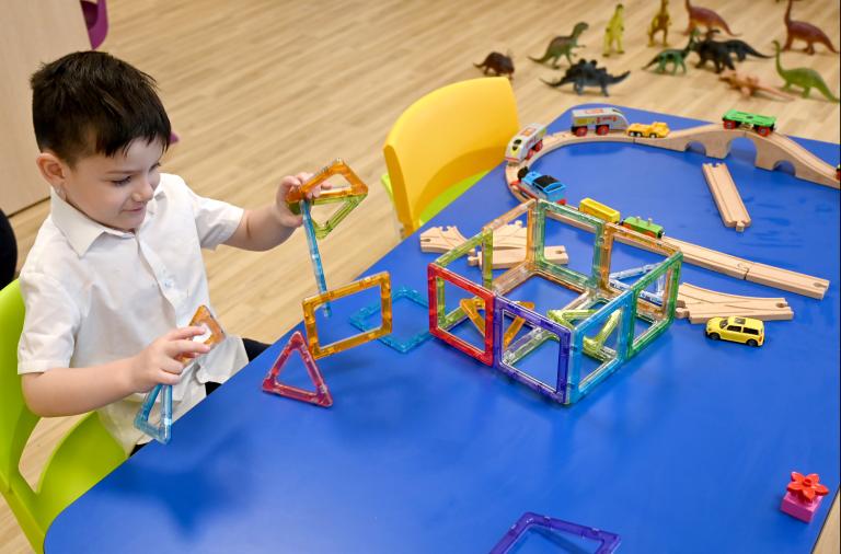 A boy sits at a table building with coloured shapes