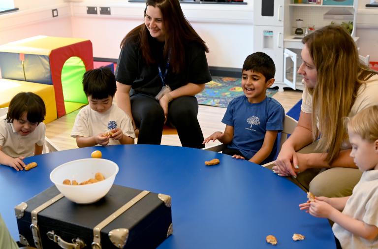 4 children and two adults sit round a table investigating items