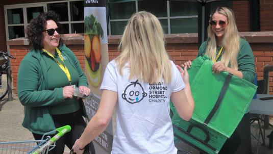 Two smiling women from the council hand a green recycling bag to a shopper from a stall outside Asda in Lower Earley