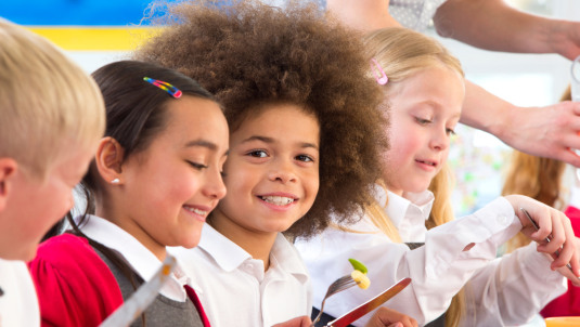 Four children in school uniform working at a table, one looking towards the camera smiling