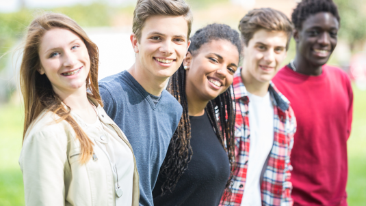 Five young people standing in a row smiling at the camera