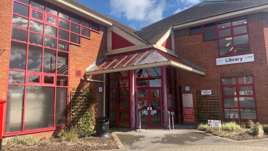 Entrance to the Wokingham library with red framed windows and doors on a red brick building