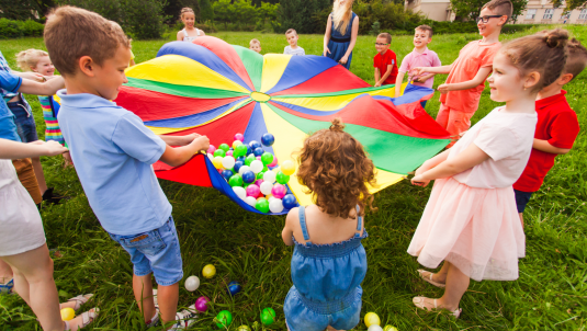 A group of children holding up a colourful parachute with balls balanced atop