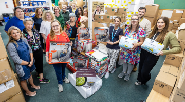 17 people from winter warmers network smile to the camera surrounded by boxes, some are holding energy efficient items